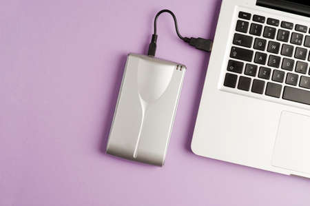 Aluminum external hard drive, partial laptop view, purple background, office concept.top viewの写真素材