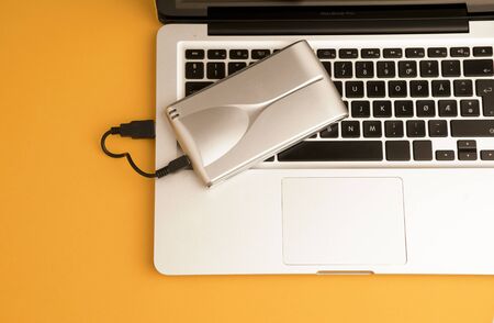 Aluminum external hard drive, partial laptop view, on orange office table.Top viewの写真素材