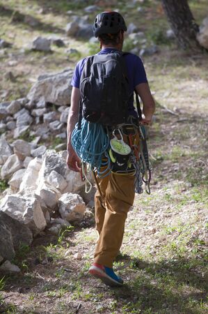 young man, with ropes, and climbing equipment walking through the countryside, rock climbing team