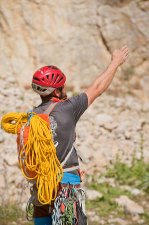 Rock climber with mountaineering accessories indicates route direction, via climbing