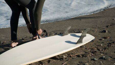 surfer preparing equipment, surfboard on the shore of the beach, with the sea in the backgroundの写真素材