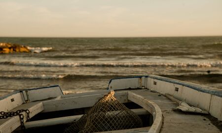 White fishing boat with fishing gear at sunset on Bournemouth beach with remote dockの写真素材
