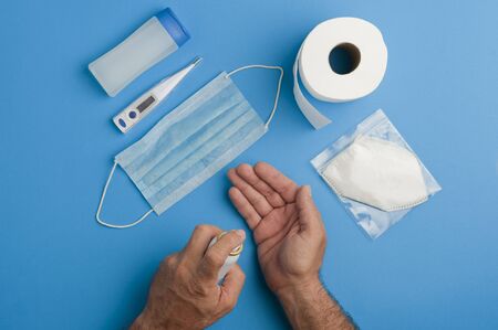covid-19 prevention concept, crossed men's hands, prevention accessories, handkerchiefs in plastic bags, gel with blue cap, digital thermometer, white mask in individual protective bag, blue mask andの写真素材