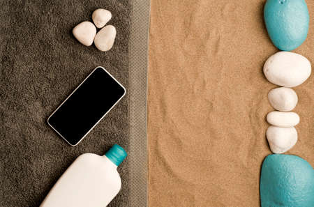 summer in the beach concept, cris towel on beach sand smartphone black screen and white cream boat, with white stones, on top of white sand and turquoise stones. beach sand .top view. space for textの写真素材