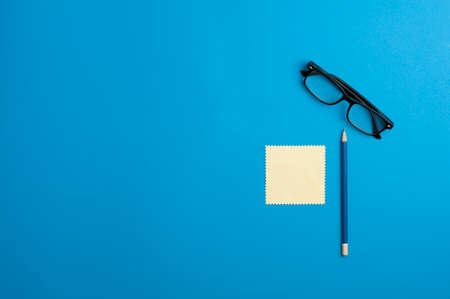 black optical glasses, blue pencil, sticky notes, on blue background.top viewの写真素材