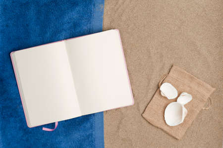 beach vacation concept, blue towel with open book, beach sand with sackcloth bag and shells on...