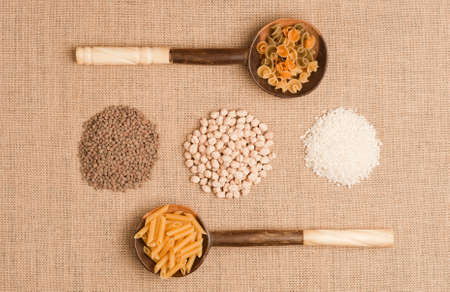 Texture or background of brown sackcloth and wooden spoons with Italian pasta on top, with rice, chickpeas and lentils.top viewの写真素材