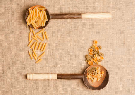Texture or background of brown sackcloth and wooden spoons with Italian pasta on linen. Top viewの写真素材