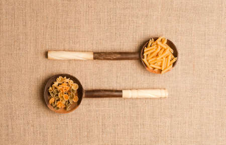 Wooden spoons with Italian pasta on background of brown sackcloth. Top viewの写真素材