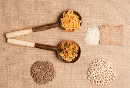Texture or background of brown sackcloth and wooden spoons with Italian pasta on top. flax sacks with rice, chickpeas and lentils.top viewの写真素材