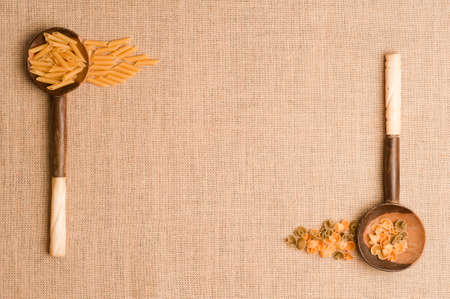 Texture or background of brown sackcloth and wooden spoons with Italian pasta on linen. Top viewの写真素材