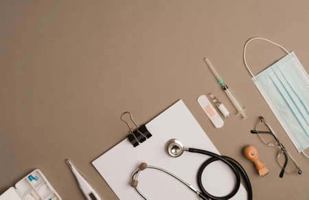 covid-19 concept (coronavirus) with medical instruments, protection material, mask, stethoscope, vaccine syringe, pillbox with capsules, glasses and notepad, brown background, top viewの写真素材