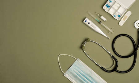 covid-19 concept (coronavirus) with medical instruments and protection material (mask, stethoscope, thermometer, syringe with vaccine, pillbox with capsules), green background, top viewの写真素材