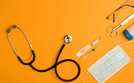 Covid-19 Coronavirus concept. medicine accessories, stethoscope, notepad and pen, orange background with copy space. top viewの写真素材
