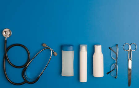 Covid-19 Coronavirus concept. alcohol gel, stethoscope, syringe with coronavirus vaccine, eyeglasses, scissors, blue background with copy space. top viewの写真素材