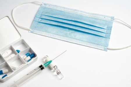 coronavirus (covid-19) vaccine concept syringe with glass container, protection mask and medicine pillbox, white background, top viewの写真素材