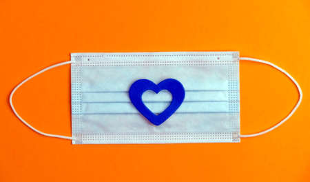 covid-19 concept, virus protection mask with blue heart, orange background, space for text. top viewの写真素材