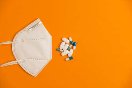 Covid-19 concept, white nk95 mask with group of white and blue pills, orange background. Top viewの写真素材