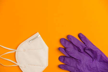 Covid-19 concept, white nk95 mask with lilac virus protection gloves, orange background. Top viewの写真素材