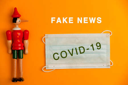 fake new concept, wooden doll, with covid-19 virus protection mask, orange backgroundの写真素材