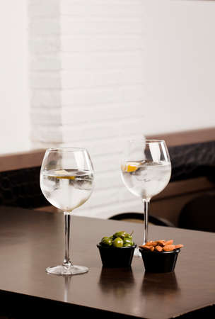 large glasses with alcoholic drink, ice and a piece of natural orange and container with olives and almonds, on top of the wooden table, inside the restaurant and free space for decoration.の写真素材