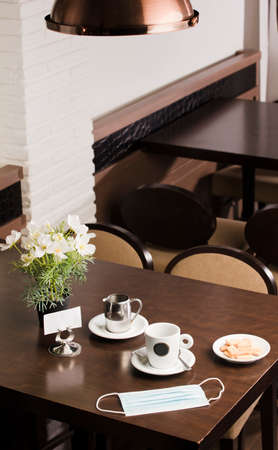 Freshly brewed hot white coffee on the wooden table inside the cafeteria with protection mask, covid-19, cookies, and metal milk jug and free space for decoration.の写真素材