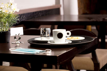 Freshly brewed hot white coffee on the wooden table inside the cafeteria with protection mask, covid-19, cookies, and metal milk jug and free space for decoration.の写真素材