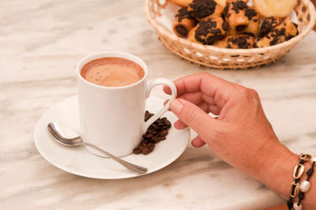 cup of coffee with woman's hand, on marble table, with pastries in wicker basketの写真素材