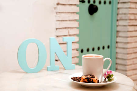 activate concept, (letters ON) cup of coffee with sweet, on marble table, with pastries in wicker basket, and background of Mediterranean house, space for textの写真素材