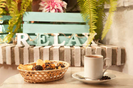 cup of coffee on marble table, (letters word relax), with pastries in wicker basket, and Mediterranean house background with plantsの写真素材