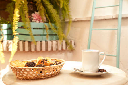 cup of coffee on marble table, with pastries in wicker basket, and Mediterranean house background with plantsの写真素材