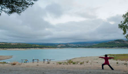 woman with curly hair, doing yoga from the back (not recognizable) with winter landscape with mountains and water,の写真素材