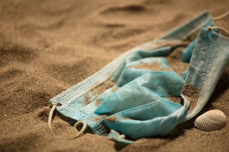 Waste during COVID-19. Discarded to single-use coronavirus face masks. Environmental pollution, on the sandy beach, at sunsetの写真素材