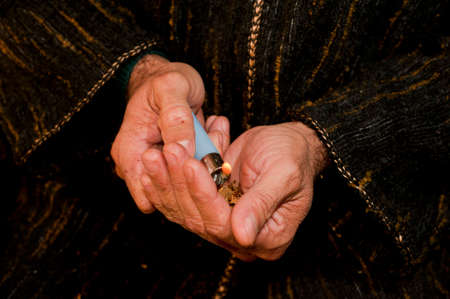 man hands with dark djellaba and fire lighter, cigar in hand, prepares hashish cigar (piece of...