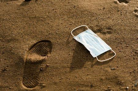 Waste during COVID-19 with footprints of man. Dumped into oceanic coronavirus single-use face masks....