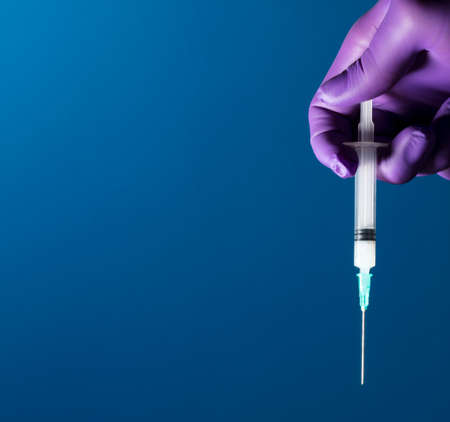Syringe, medical injection in the hand, palm or fingers. Plastic vaccination kit with needle. Nurse or doctor. Liquid or narcotic drugs. Health care in hospital Blue backgroundの写真素材