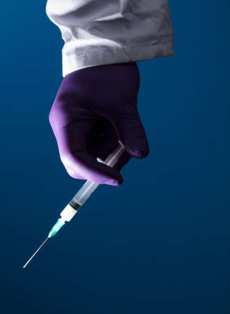 Syringe, medical injection in the hand, palm or fingers. Plastic vaccination kit with needle. Nurse or doctor. Liquid or narcotic drugs. Health care in hospital Blue backgroundの写真素材