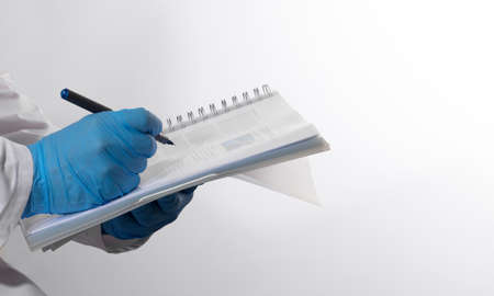 Male doctor on duty in white coat reading patient information with pen in hand, filling prescription...