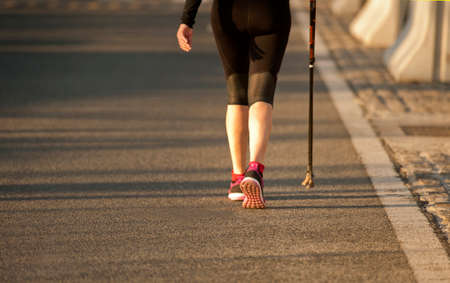 woman walking with black pants and trekking poles on asphalt cityの写真素材