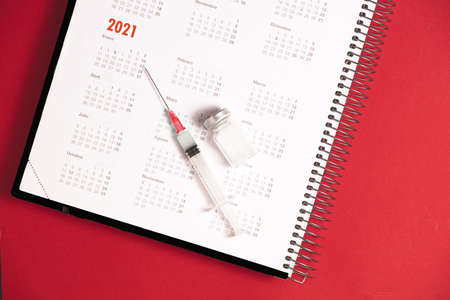 syringe and vaccine with calendar 2021, red backgroundの写真素材