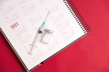 syringe and vaccine with calendar 2021, red backgroundの写真素材