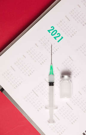 syringe and vaccine with calendar 2021, red backgroundの写真素材