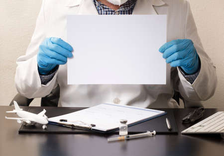 Doctor with blue gloves, white poster in hands (to fill out), desk with syringe, vaccine, airplane,...