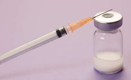 medical syringe cannula with vaccine vial, lilac background. macro