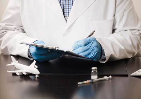 hand of doctor with pen filling in data, on form, with passenger plane, syringe ,, computer...