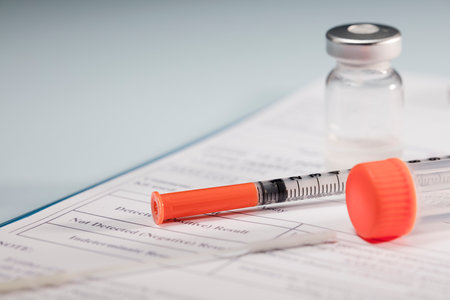 syringe and vaccine, orange closure transparent vial transport tube over medical report folder and soft blue backgroundの写真素材