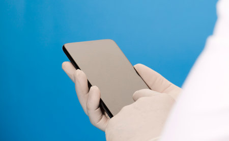 phone in the hands of a doctor (telephone assistance) with surgical glove and blue backgroundの写真素材