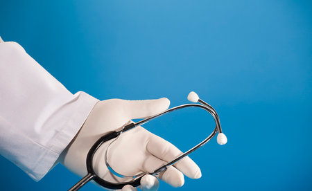 Stethoscope in doctor's hand with surgical glove and blue background.の写真素材