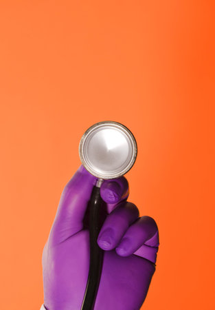 stethoscope in the hands of a doctor with lilac surgical gloves and orange backgroundの写真素材