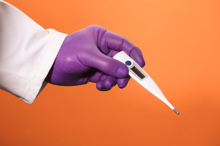 thermometer in the hands of a doctor with lilac surgical gloves and orange backgroundの写真素材